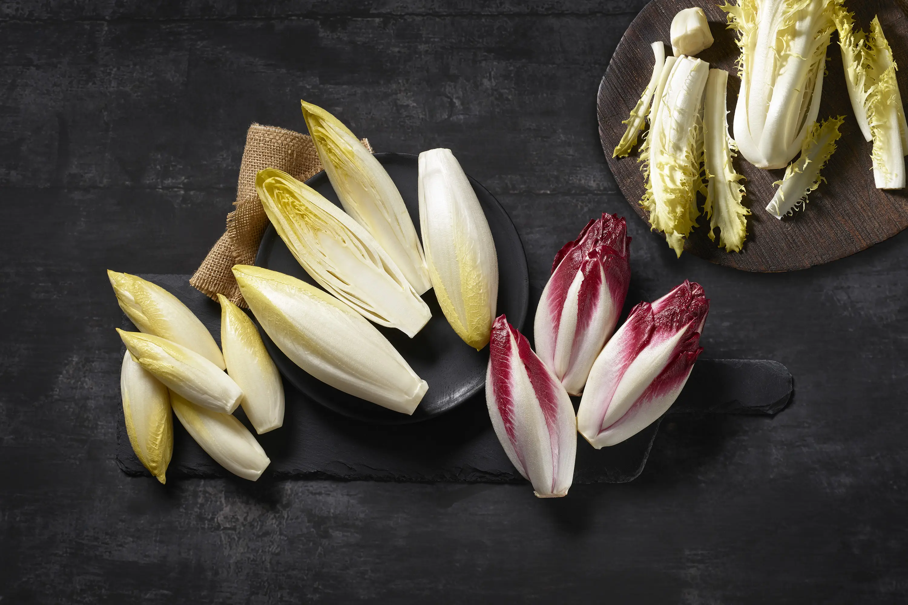 4 Sorten Chicorée: Weißer, roter, Chicorette Mini-Chicorée und Friseline, arrangiert auf einem Holzbrett