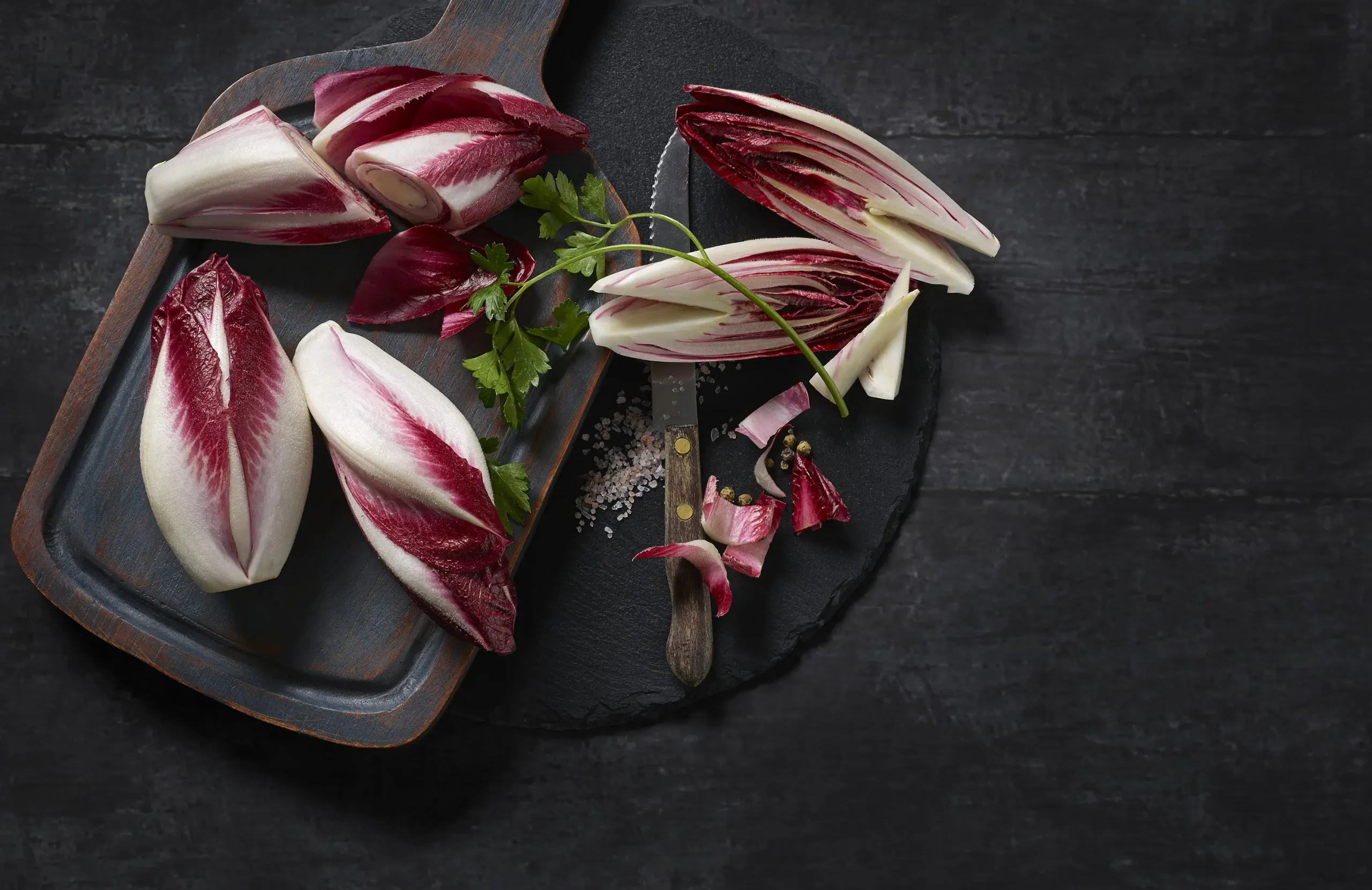 Roter Chicorée, aufgeschnitten auf einem Schiefer-Brett, dekoriert mit Salz, Petersilie