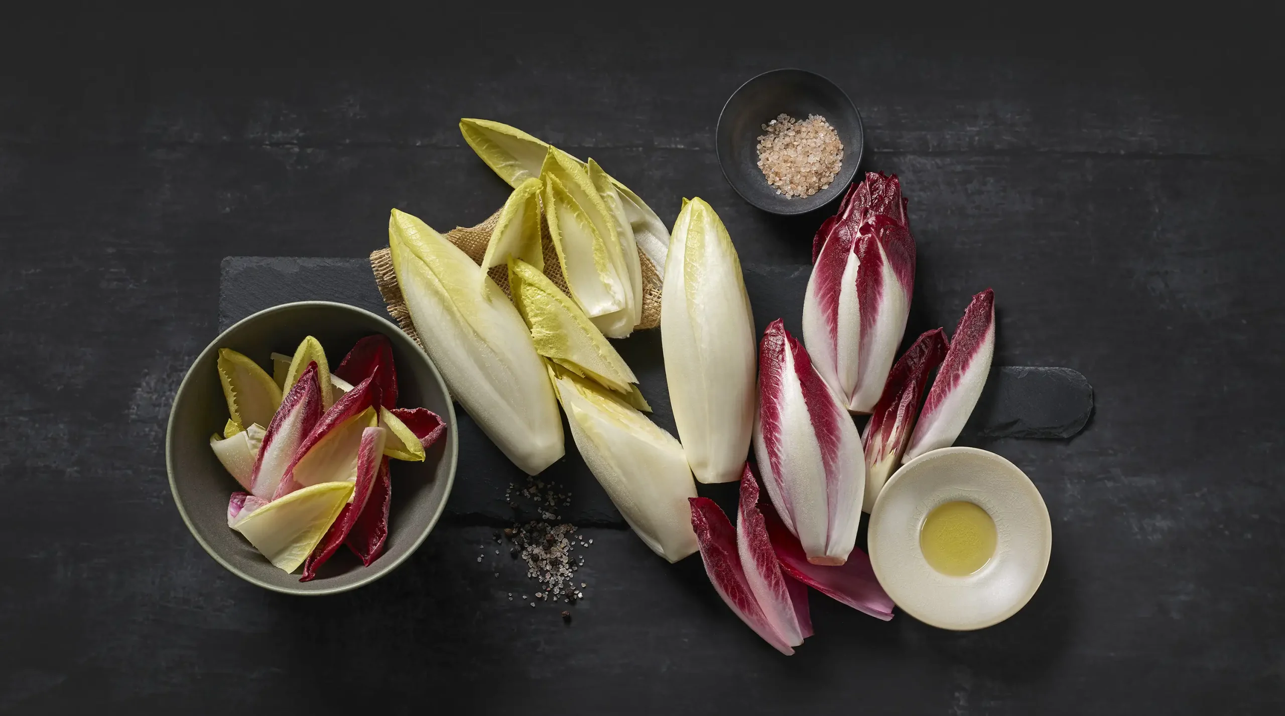 2 Sorten Chicorée (weiß, rot) kulinarisch präsentiert auf dunklem Hintergrund