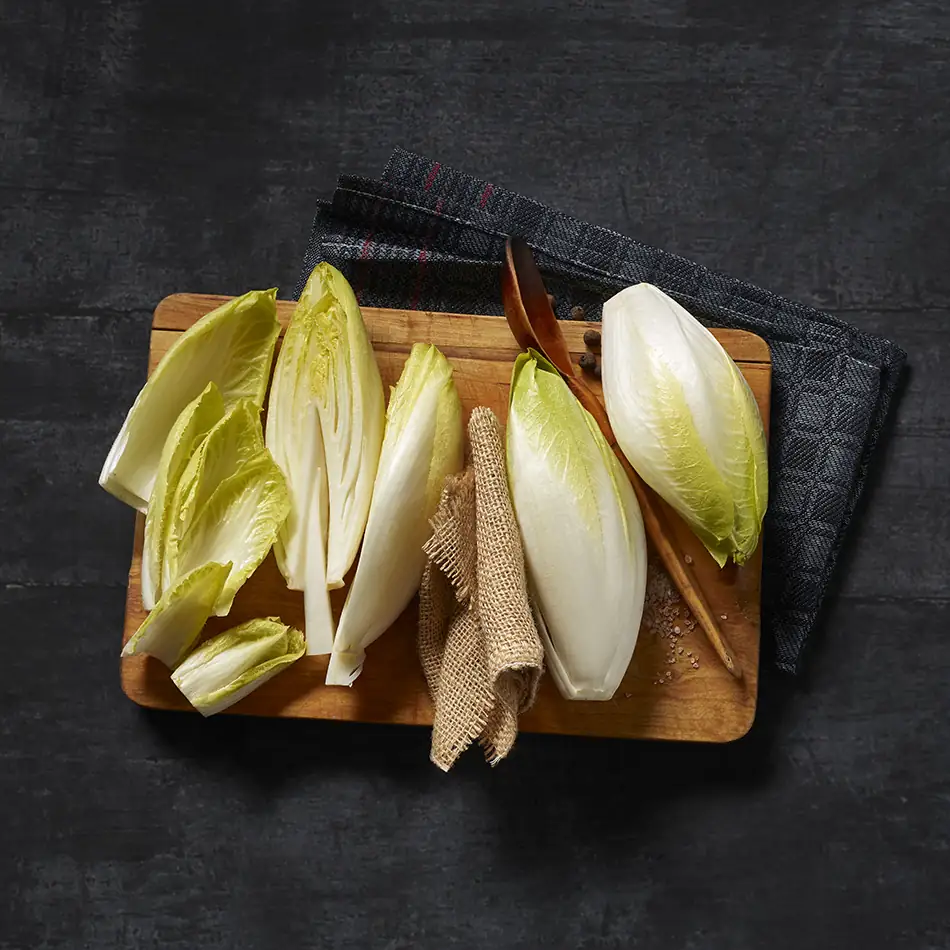 Več kosov bele cikorije, ki jih razporedite na leseno desko, delno razpolovite in izrežite steblo.