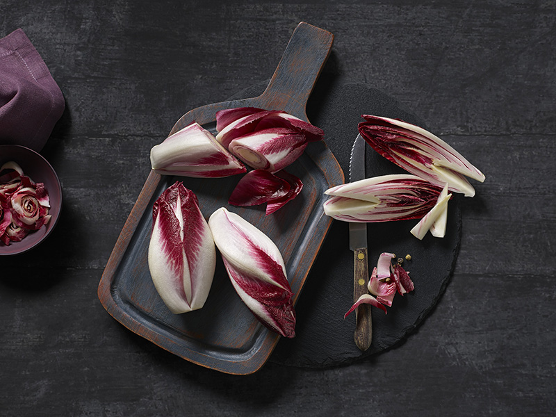 Mehrere Stück roter Chicorée auf einem Holzbrett. Teilweise aufgeschnitten, Strunk entfernt
