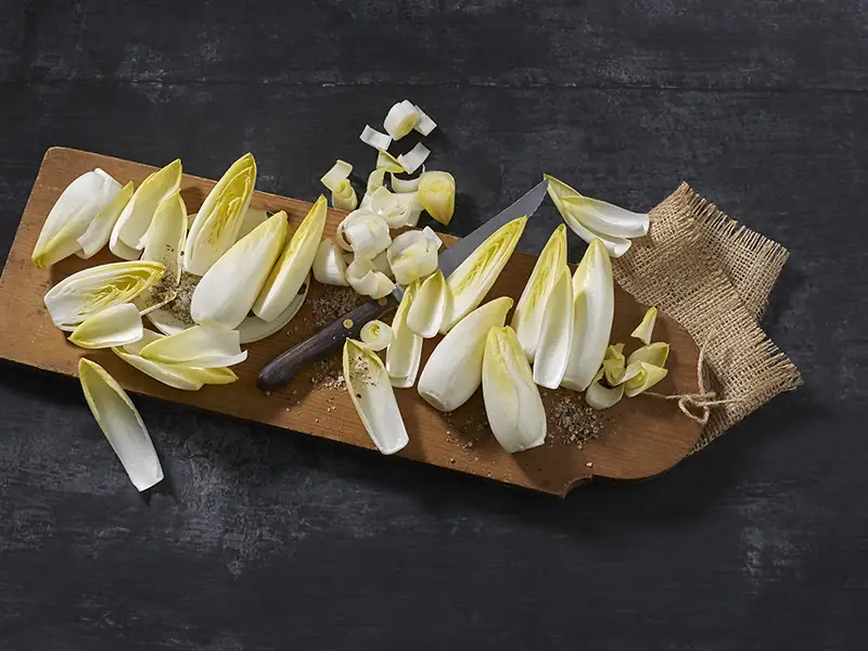 Chicorette Mini Chicorée – mehrere Stück, teilweise aufgeschnitten, auf einem länglichen Holzbrett